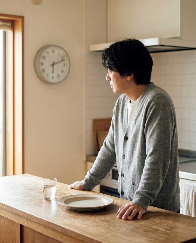 A thoughtful person glancing at a wall clock near an empty plate